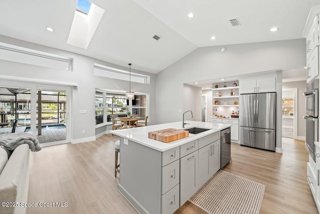 kitchen with appliances with stainless steel finishes, a skylight, sink, hanging light fixtures, and a kitchen island with sink