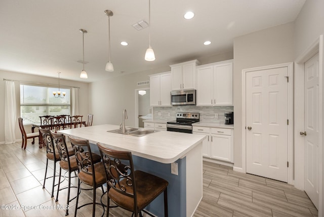 kitchen featuring sink, white cabinets, hanging light fixtures, a center island with sink, and appliances with stainless steel finishes