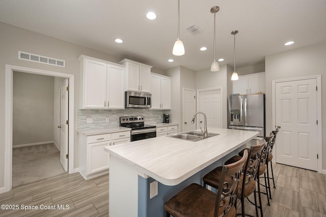 kitchen with decorative light fixtures, stainless steel appliances, a center island with sink, white cabinetry, and sink