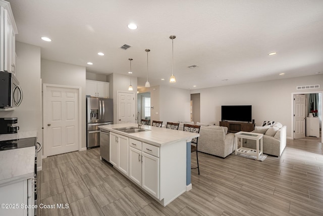 kitchen with a center island with sink, stainless steel appliances, hanging light fixtures, sink, and white cabinetry