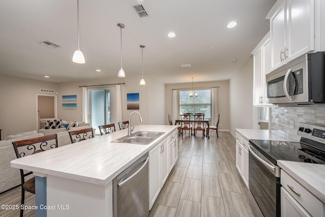 kitchen featuring a kitchen breakfast bar, a kitchen island with sink, appliances with stainless steel finishes, sink, and decorative light fixtures