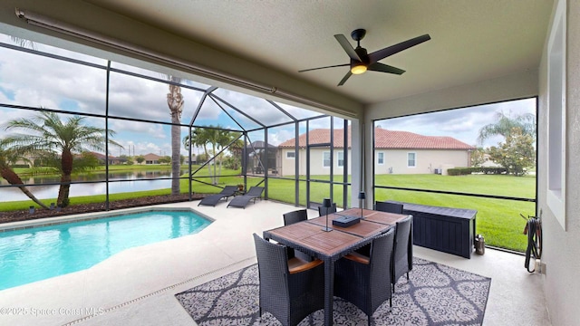 view of pool featuring glass enclosure, ceiling fan, a yard, a water view, and a patio