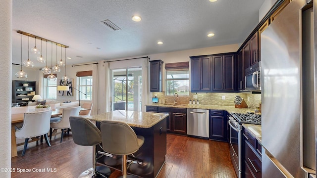 kitchen with backsplash, hanging light fixtures, light stone countertops, appliances with stainless steel finishes, and a kitchen island