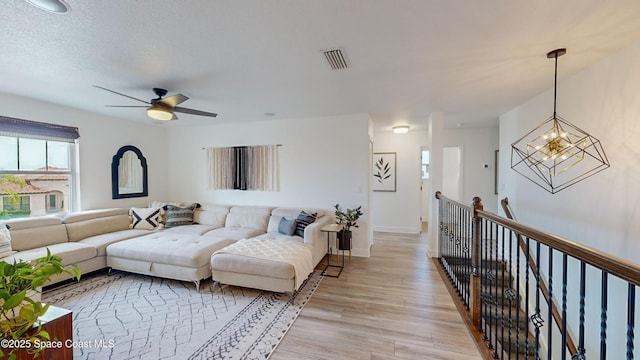 living room with a textured ceiling, ceiling fan with notable chandelier, and light hardwood / wood-style flooring