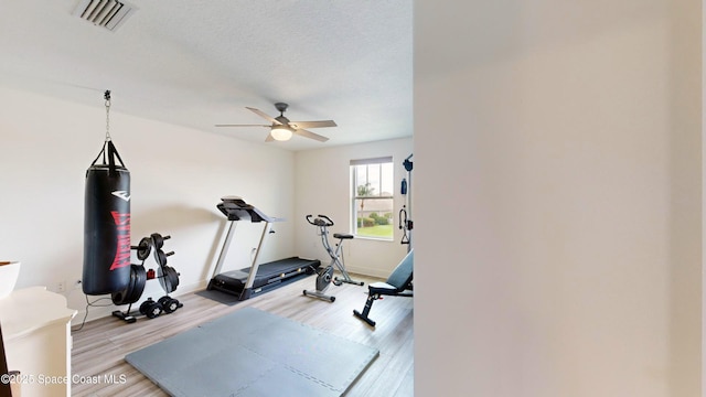 exercise room with a textured ceiling, light hardwood / wood-style flooring, and ceiling fan