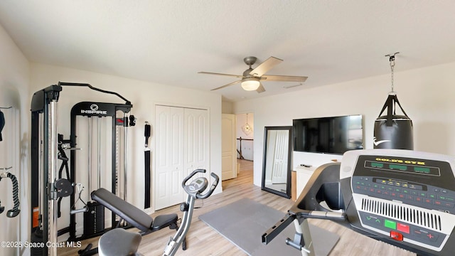 workout area with ceiling fan, light hardwood / wood-style flooring, and a textured ceiling