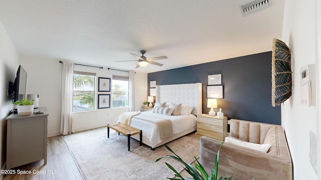 bedroom featuring ceiling fan, light hardwood / wood-style flooring, and a textured ceiling