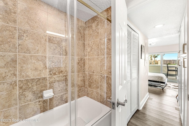 bathroom featuring a textured ceiling, bath / shower combo with glass door, and hardwood / wood-style floors