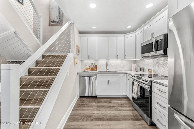 kitchen featuring sink, stainless steel appliances, light hardwood / wood-style floors, decorative backsplash, and white cabinets