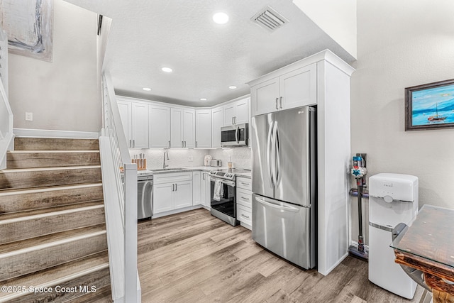 kitchen featuring white cabinetry, sink, stainless steel appliances, tasteful backsplash, and light wood-type flooring