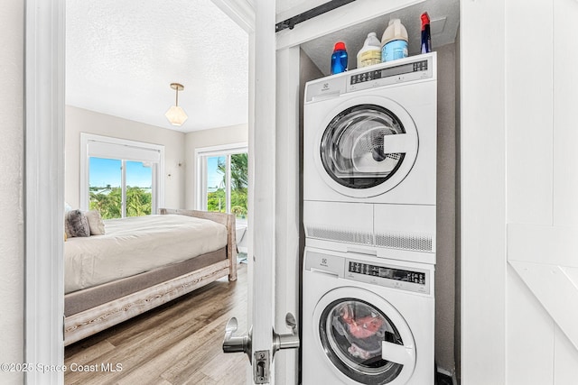 laundry area with wood-type flooring, a textured ceiling, and stacked washer / dryer