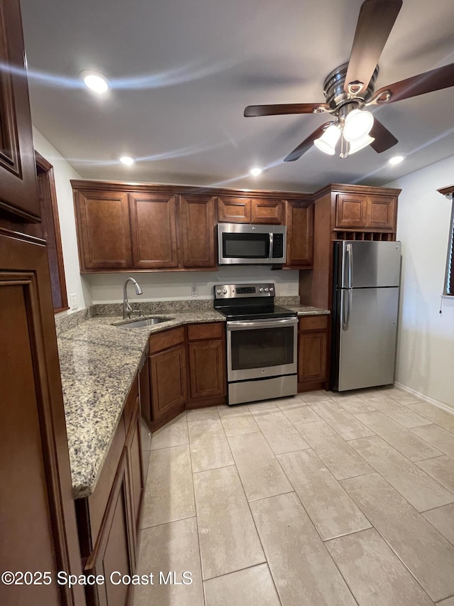 kitchen featuring light stone countertops, appliances with stainless steel finishes, sink, ceiling fan, and light tile patterned floors