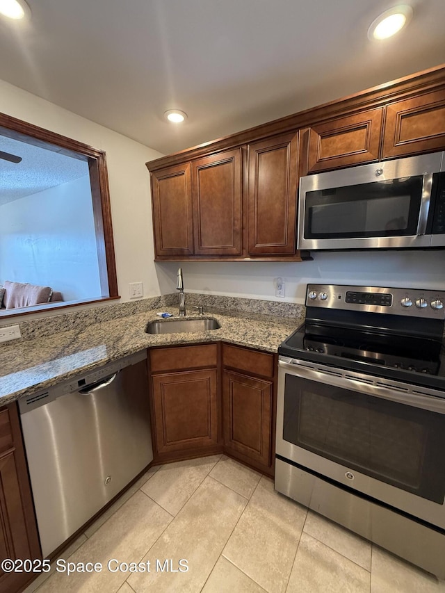 kitchen with light tile patterned floors, light stone countertops, sink, and stainless steel appliances