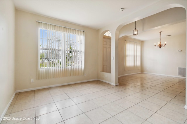 tiled spare room featuring a notable chandelier