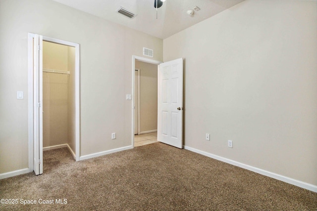 unfurnished bedroom featuring a closet, a walk in closet, light colored carpet, and ceiling fan