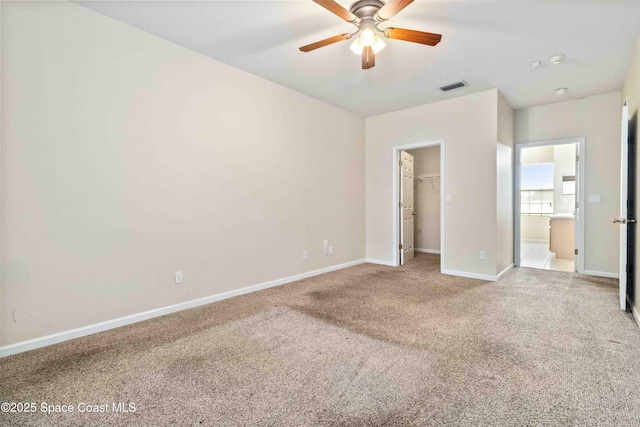 unfurnished bedroom featuring a walk in closet, a closet, carpet flooring, ceiling fan, and ensuite bathroom