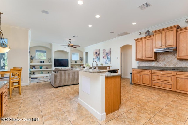 kitchen featuring hanging light fixtures, ceiling fan, an island with sink, and ornamental molding