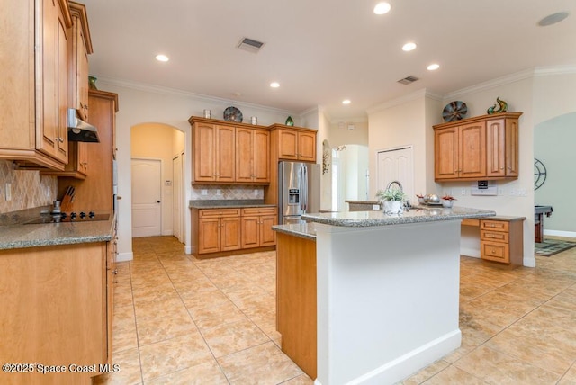 kitchen with a kitchen island with sink, stainless steel fridge, decorative backsplash, and crown molding