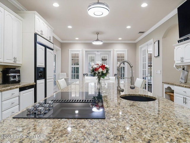 kitchen with light stone countertops, black electric stovetop, white cabinets, and sink