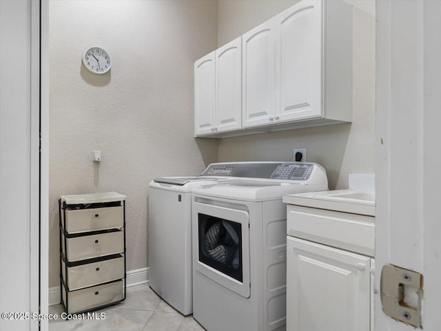 clothes washing area featuring washer and dryer, light tile patterned floors, and cabinets