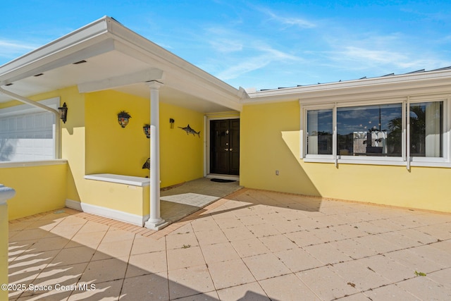 view of exterior entry with a garage, a patio, and stucco siding