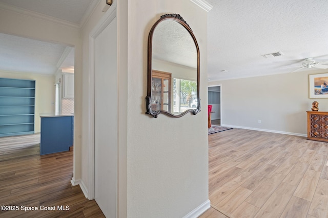 corridor with a textured ceiling, light wood-type flooring, and ornamental molding