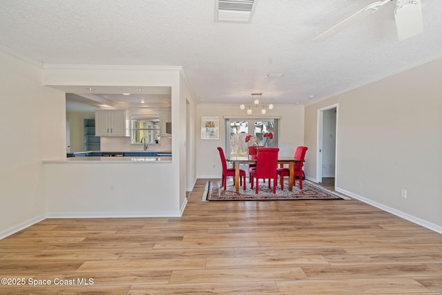 dining room with light hardwood / wood-style floors, crown molding, a textured ceiling, an inviting chandelier, and sink