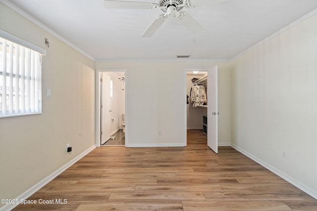 unfurnished bedroom with connected bathroom, baseboards, a spacious closet, ornamental molding, and light wood-type flooring