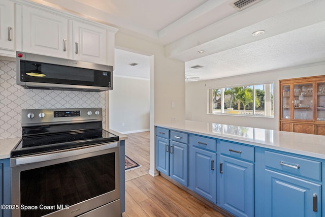 kitchen featuring stainless steel appliances, light wood-type flooring, white cabinets, blue cabinets, and backsplash