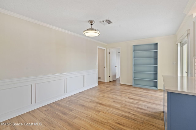 unfurnished dining area with ornamental molding, a textured ceiling, light wood-type flooring, and built in features