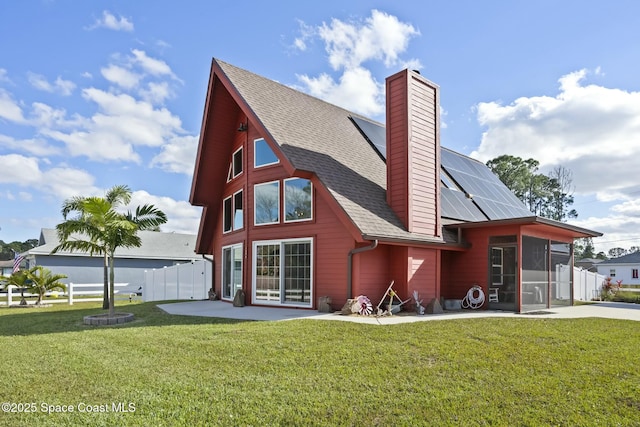 rear view of house with a sunroom, a yard, a patio, and solar panels