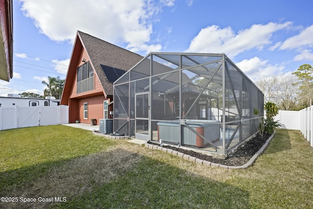 rear view of house with glass enclosure, cooling unit, a yard, and a hot tub