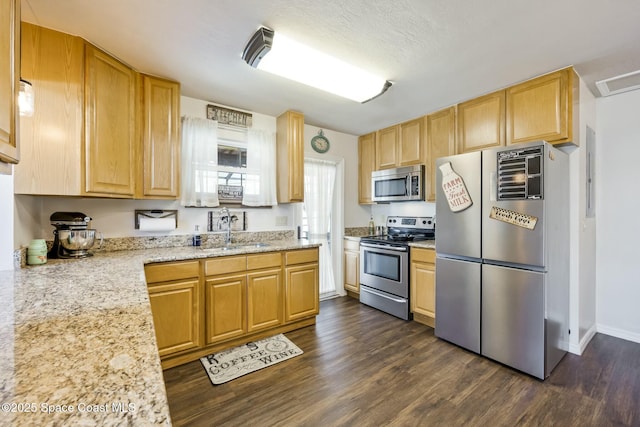 kitchen featuring sink, light brown cabinets, dark wood-type flooring, stainless steel appliances, and light stone counters