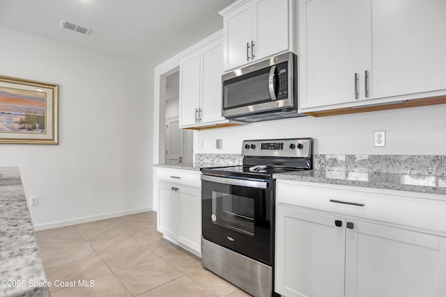 kitchen with stainless steel appliances, white cabinets, a textured ceiling, light stone counters, and light tile patterned floors