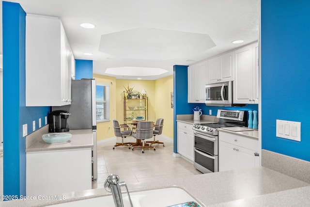 kitchen with stainless steel appliances, white cabinetry, sink, and a tray ceiling