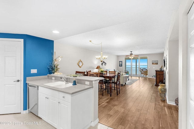 kitchen with stainless steel dishwasher, light hardwood / wood-style floors, white cabinetry, ceiling fan with notable chandelier, and sink