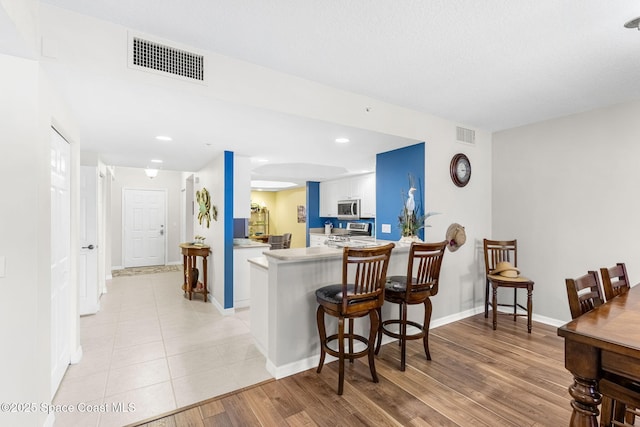 kitchen featuring stainless steel appliances, white cabinetry, a kitchen breakfast bar, light wood-type flooring, and kitchen peninsula