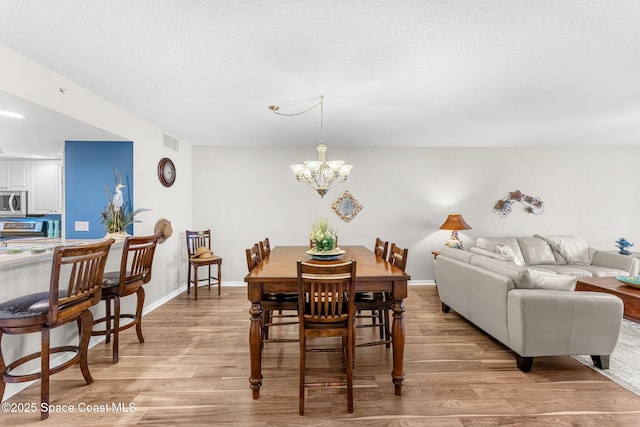 dining area with a textured ceiling, a chandelier, and light hardwood / wood-style flooring