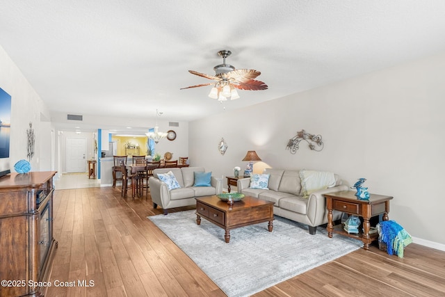 living room featuring ceiling fan with notable chandelier and light wood-type flooring