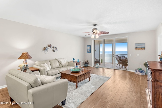 living room with ceiling fan, light hardwood / wood-style floors, and a water view