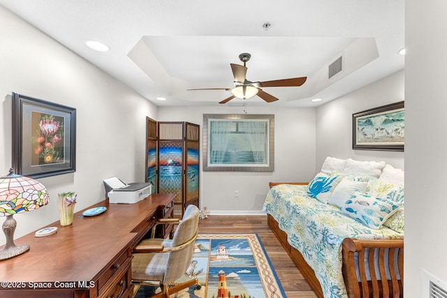 bedroom featuring ceiling fan, dark hardwood / wood-style floors, and a tray ceiling