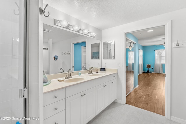 bathroom with a textured ceiling, hardwood / wood-style floors, a shower with shower door, ceiling fan, and vanity