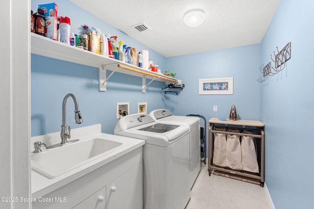 washroom featuring a textured ceiling, light tile patterned floors, cabinets, washing machine and clothes dryer, and sink