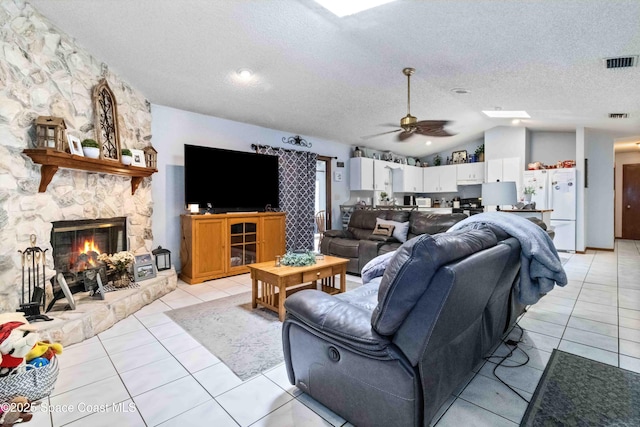 living room with ceiling fan, vaulted ceiling, a stone fireplace, and a textured ceiling