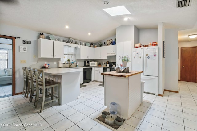 kitchen with a textured ceiling, white cabinets, black appliances, and lofted ceiling with skylight