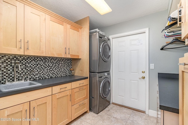 clothes washing area featuring cabinets, light tile patterned floors, a textured ceiling, sink, and stacked washer and dryer