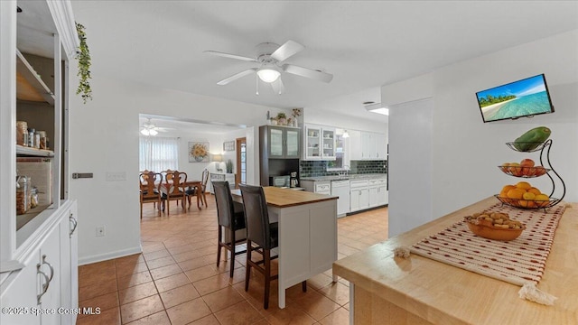 kitchen featuring ceiling fan, decorative backsplash, white dishwasher, a kitchen breakfast bar, and white cabinets