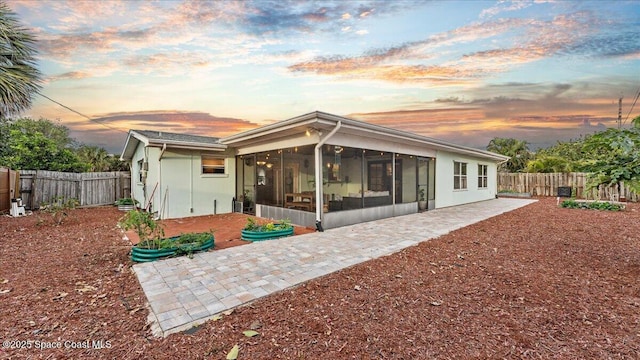 back house at dusk with a sunroom and a patio