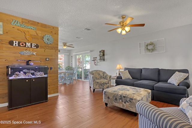 living room with a textured ceiling, ceiling fan, wood-type flooring, and wooden walls