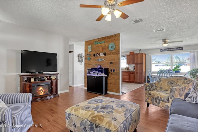 living room featuring ceiling fan, a textured ceiling, and light hardwood / wood-style flooring